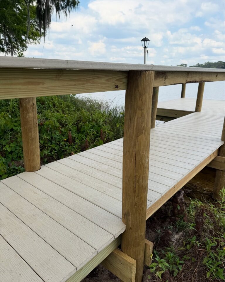 Wooden dock or boardwalk by the water with railing posts and a cloudy blue sky in the background