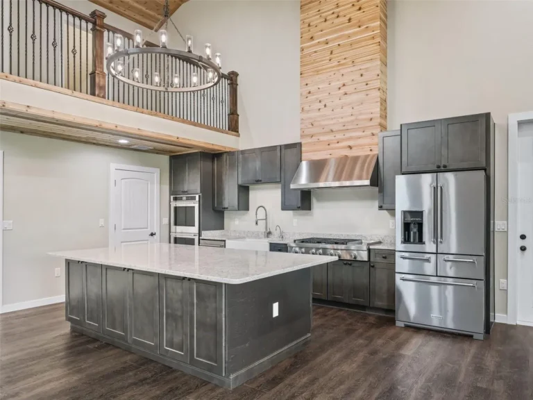Modern kitchen with dark cabinets, quartz island, stainless steel appliances, and a wooden beam/column extending to a second-floor railing.